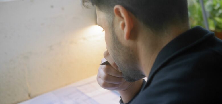 A man sitting at a desk, holding a pen, focused on proofreading a document with a desk lamp illuminating his work